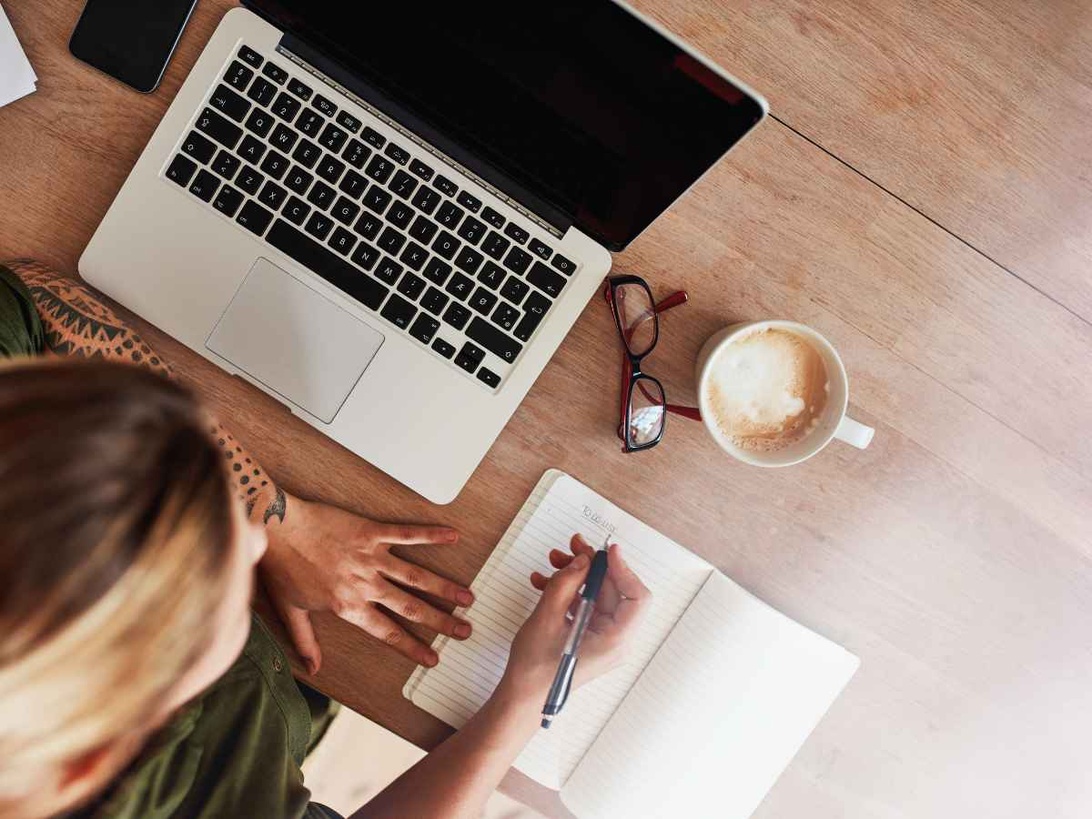 En bloggares arbetsplats med laptop, anteckningsbok och kaffekopp, vilket visar det praktiska arbetet bakom en blogg.